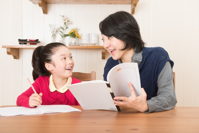 宿題をする女の子と勉強を教える母親
