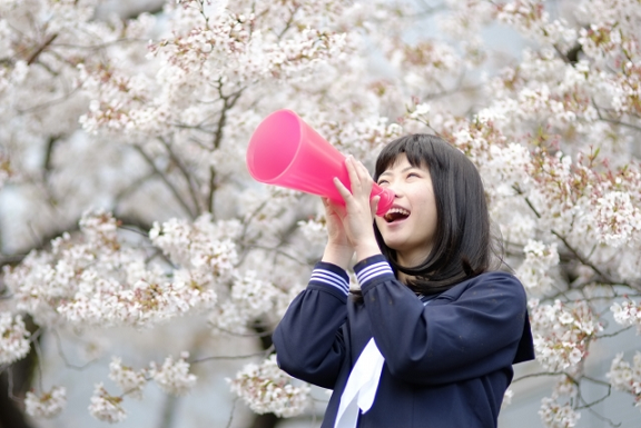 桜の木の下でメガホンを持つ女子学生